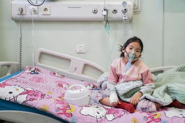 A young girl sitting on a hospital bed and wearing an oxygen mask