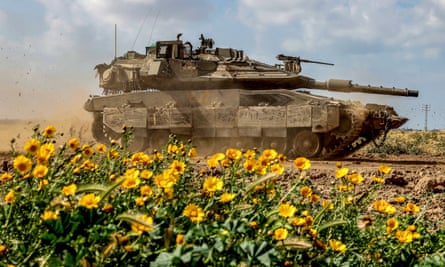 An Israeli tank, set against the backdrop of a blue sky, sits near yellow wildflowers along Israel’s southern border with the Gaza Strip