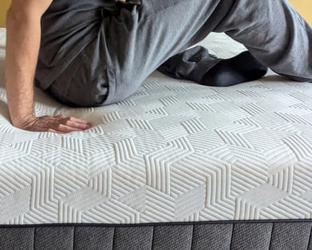 A person is seen sitting fully on the mattress and pushing their right hand into the Panda Hybrid bamboo mattress which has a tessellating design. The person is cropped at the waist.