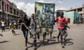 A group of young men carrying a banner showing two soldiers in front of a DRC flag, run through the streets