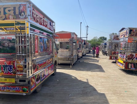 Two women walking between two rows of shiny trucks covered in gaudy colours, writing in Hindi and photos