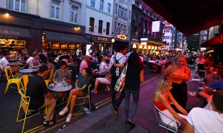 A street full of chairs and tables outside cafes with people dining after dark