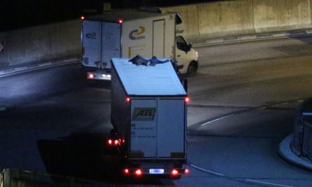 Two migrants cling to the roof of a freight lorry as it leaves the Eurotunnel terminal.