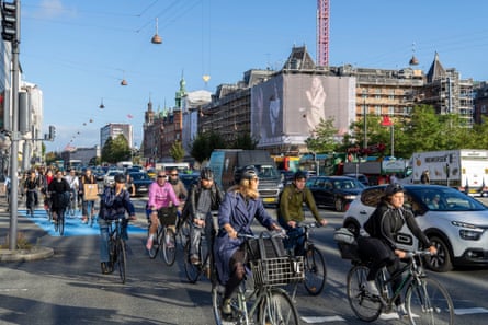 Men and women riding their bicycles through Copenhagen city centre in a dedicated cycle lane alongside cars.
