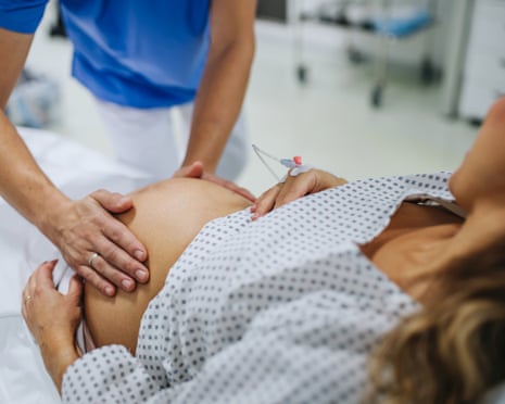 Obstetrician examining pregnant woman in hospital, touching woman’s belly
