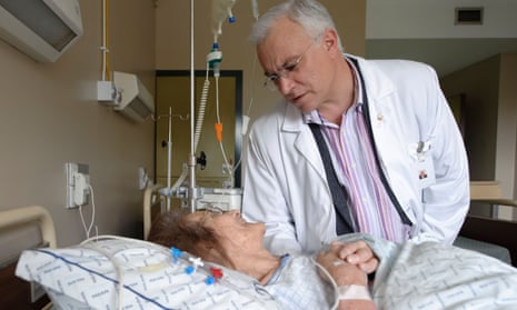 Male doctor tending to elderly female patient on a drip in a hospital bed
