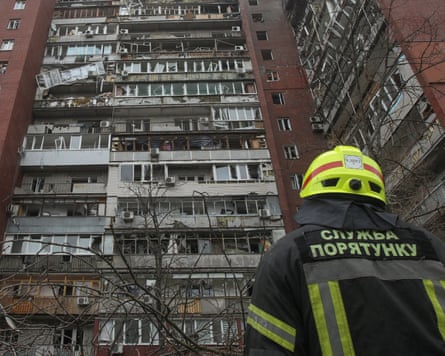 A firefighter with their back to the camera looks up at a damaged high-rise building