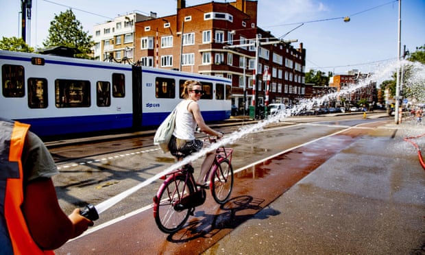 A firefighter sprays water as a woman rides her bicycle during the recent heatwave in Amsterdam.