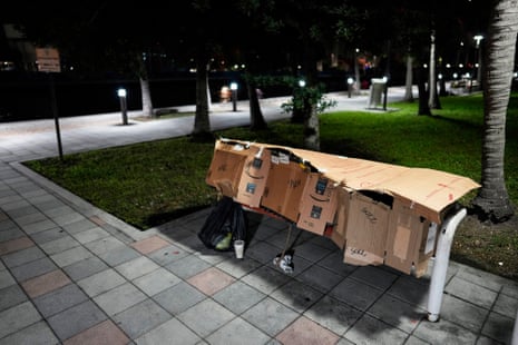 A person sleeps inside a makeshift shelter on park bench
