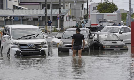 A man in front of partially submerged cars on a flooded road in Toyokawa, in central Japan’s Aichi prefecture, on Saturday