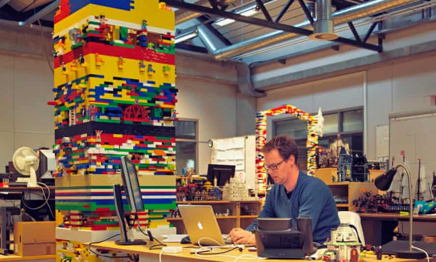 A man at a desk with a Lego tower next to the desk