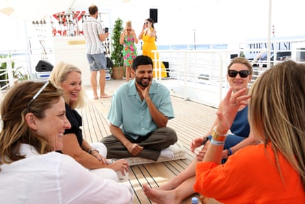 Indian man sits on wooden deck of yacht in small circle of white women.
