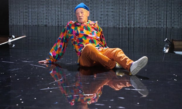 Ian McKellen as Hamlet in patchwork top, orange trousers and blue beanie hit, sat on the floor of the Ashton Hall stage