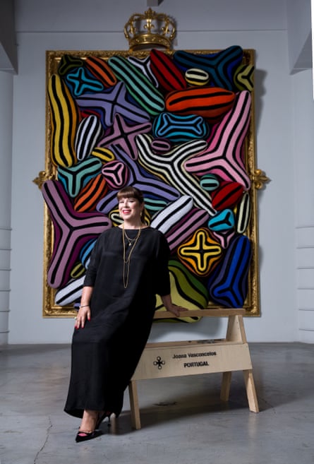 A woman in a black dress stands in front of a colourful artwork