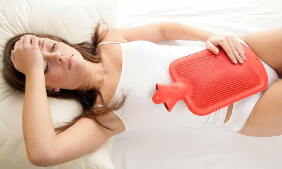 Young woman lying on bed with hot water bottle on her stomach