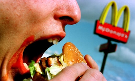Eating a Big Mac hamburger with a McDonalds sign in the background.