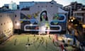 The floodlit football pitch of Las Madres Dragonas de Lavapiés in Madrid. The club plays under a mural that has the message: ‘Socially equally, totally free’.