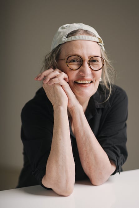 Anne Geddes, wearing a black shirt and a white baseball cap turned backwards, leans her elbows on a counter, her arms clasped and intertwined, resting on her face
