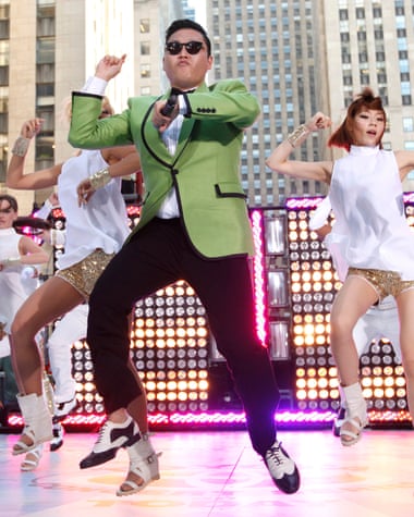 Sai in a bright green jacket and sunglasses dances on stage with two dancers