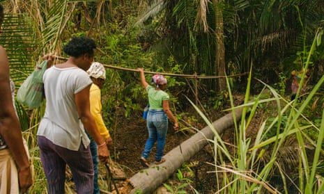 Four black women cross a tree-trunk bridge in a dense forest