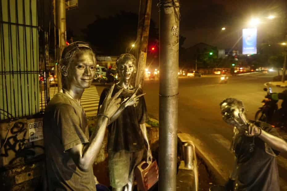 Three boys with silver paint on their bodies, also known as “Silverman” seen begging for money on a street in, Jakarta, Indonesia. Silver man, paint.