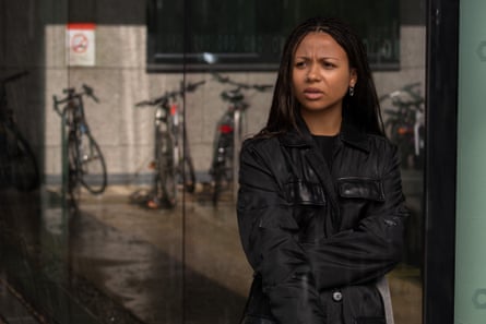 A young Black woman dressed in black standing in a street with bicycles in a rack behind her