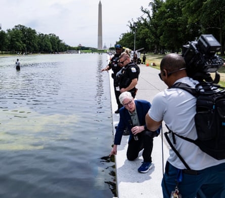 Reporters, camera operators and park employees gather around the reflecting pool with the Washington monument in the background.