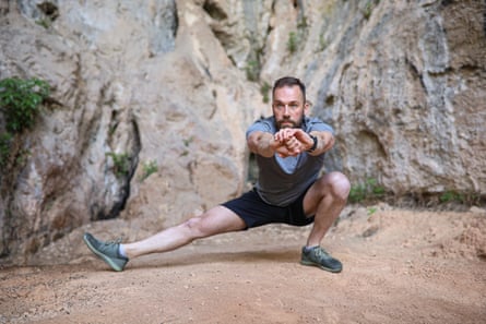 A man doing a cossack squat – one leg squatting in the normal fashion, foot flat on the ground, the other at full stretch, toes pointing up, heel on the ground