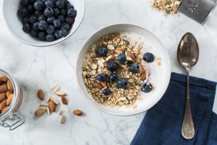 A bowl of muesli topped with nuts and blueberries and extra blueberries and nuts at the side.