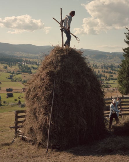 A man with a hay fork on top of a haystack while another man forks hay below
