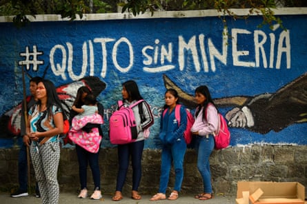 A group of Waorani Indigenous women and girls protest in front of a wall with a mural. One woman has paint across her eyes in the Amazonian style