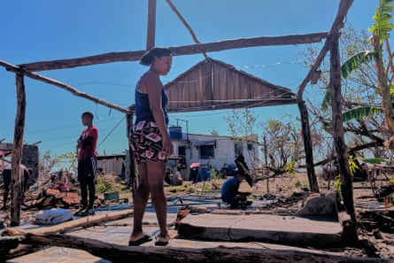 A family stand around the frame of a small hut with storm wreckage around them