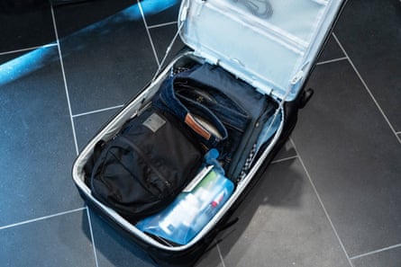 An open suitcase with belongings sits on tile floor