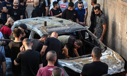 Lots of people crowd around a burnt out car