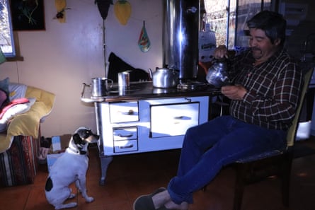 Pedro Aguilar sits at a small stove, while a dog watches him pour maté from a silver pot.