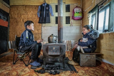 A boy and girl sitting either side of a rudimentary coal-burning stove