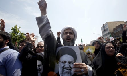 A man holding a black and white picture of a smiling Raisi stands with his fist in the air