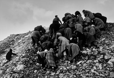 Coal scavengers in coats bend over, picking through a rocky slope of rubble