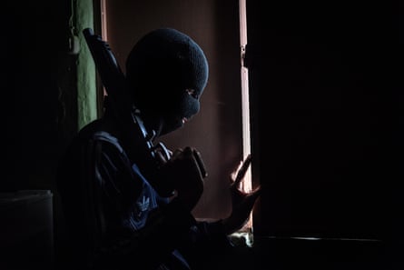 A member of a kidnapping gang watches through the window to avoid a potential police raid. He is 15 years old and joined the gang to support his family