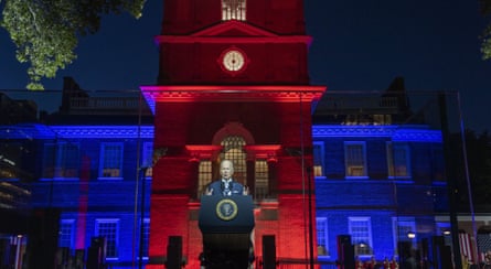Joe Biden delivers speech against a building lit up in blue and red