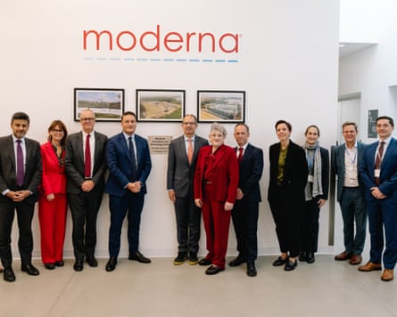 People gather in front of a white backdrop with framed pictures and Moderna company logo