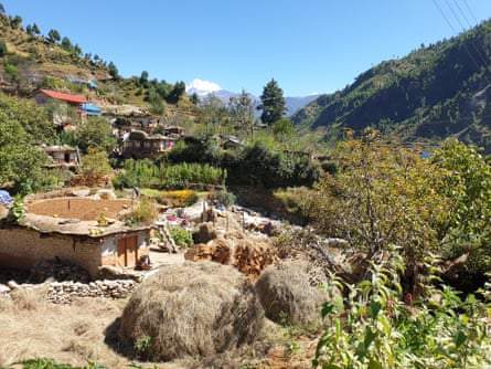 Haystacks on a hillside near a few houses surrounded by trees and shrubs.