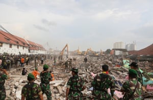 Soldiers watch as diggers move among the demolition rubble