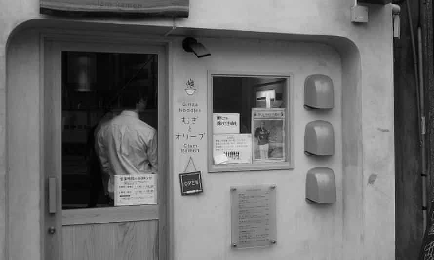 Black and white exterior of shop, with client's back seen through window of door of Mugi To Olive shop
