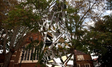 A tall abstract sculpture resembling a fall of leaves or snowflakes, against the backdrop of a large handsome church