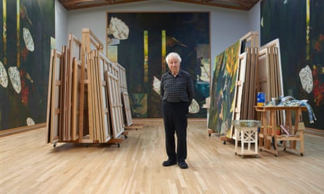 Ilya Kabakov standing in a studio with works on the walls and stacked on trolleys
