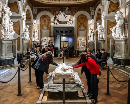 People wearing latex gloves stand within the barriers around the Veiled Christ to touch it