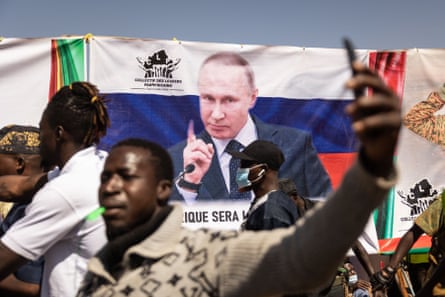 Young men demonstrate in front of a banner showing the Russian flag and Putin wagging a finger