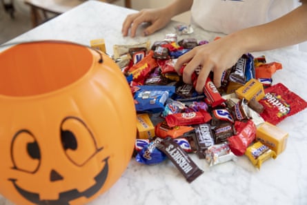 A child rifles through a pile of candy next to a jack-o’-lantern candy bucket.