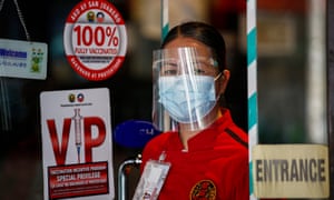 A woman wears a face mask and face shield while waiting for customers at the entrance of a shop in Manila, Philippines.